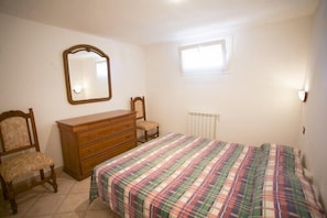 A bedroom with a bed, a wooden dresser, a chair, a mirror, and a window.