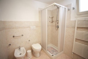 A bathroom with a shower, toilet, bidet, and a towel rack.