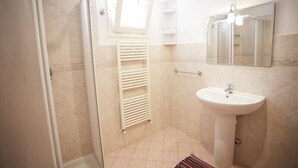 A bathroom with a shower, a sink, a towel rack, and a mirror. - Appartamento Il Cannucciato (Portoferraio)
