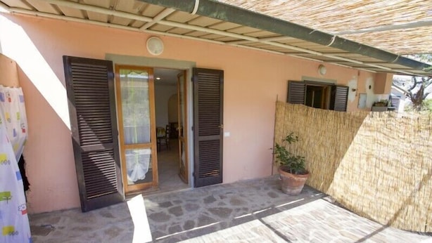 A house with a stone patio, a covered entrance, and a potted plant. - Appartamento Il Cannucciato (Portoferraio)