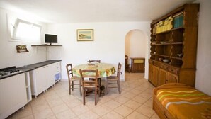 A compact kitchen with a dining table, chairs, a TV, and a small cabinet. - Appartamento Il Cannucciato (Portoferraio)