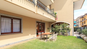 A two-story building with a balcony, a small patio with a table and chairs, and a well-maintained lawn. - Impero House Rent - Adelaide (Stresa)