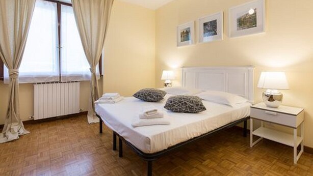 A bedroom with a bed, bedside tables, a window with curtains, and wall-mounted pictures. - Impero House Rent - Adelaide (Stresa)