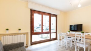 A living room with a sofa, a dining table with chairs, a TV, and a sliding glass door with a view of the outside. - Impero House Rent - Adelaide (Stresa)