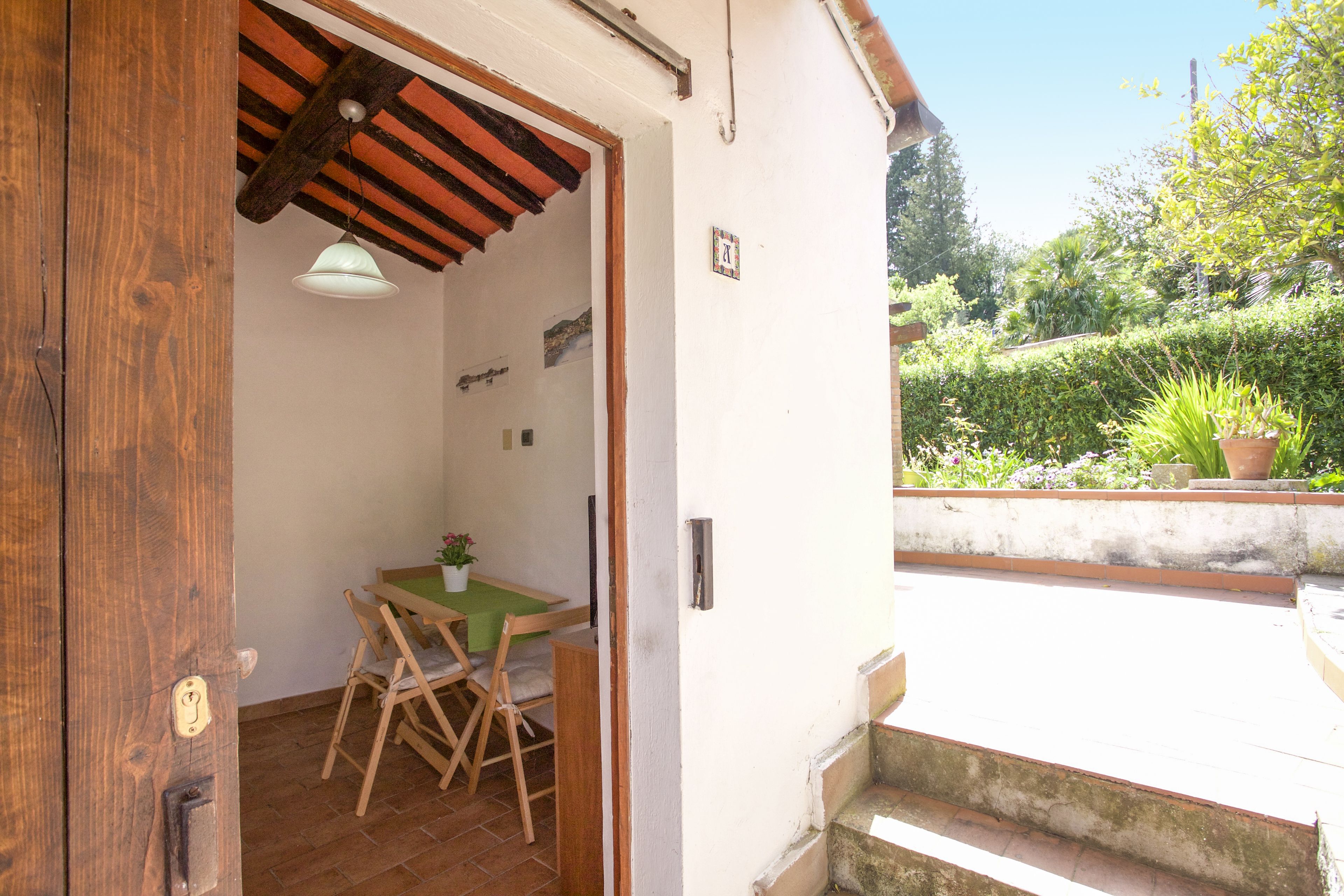 A wooden door leading to a room with a table and chairs, a hanging light fixture, and a small window with a view of a garden.