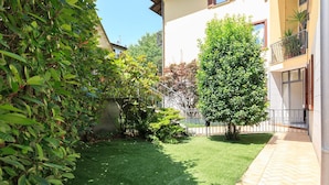 Un giardino curato con prato, arbusti vari e un albero alto.