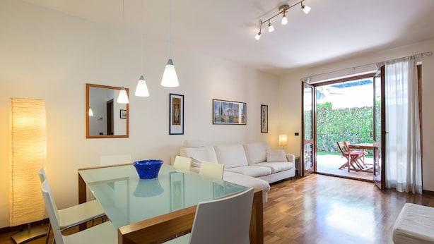 Un soggiorno moderno con tavolo da pranzo in vetro, divani bianchi e vista su un giardino attraverso ampie porte scorrevoli.