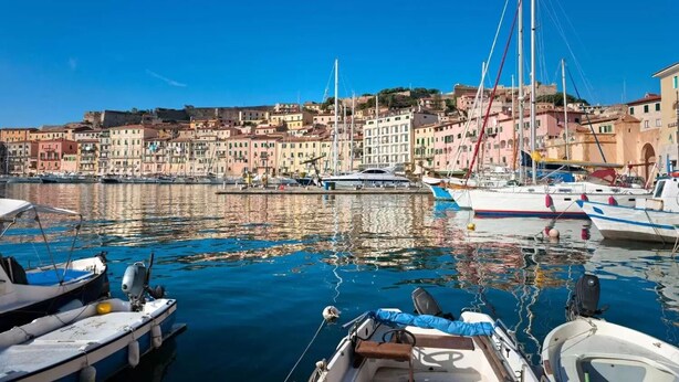 A marina with boats docked, a clear blue sky, and colorful buildings in the background. - Appartamento Bilo San Rocco (Portoferraio)
