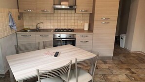 A compact kitchen with a gas stove, oven, and a dining table with chairs. - Appartamento Bilo San Rocco (Portoferraio)