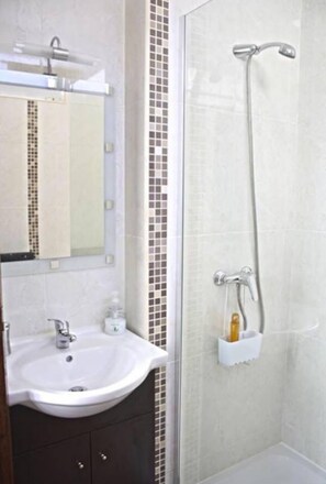 A bathroom with a white sink, a mirror, a shower with a handheld showerhead, and a soap dispenser. - Casa Azul d'Altamira with terrace historic center of Viana do Castelo  (Viana do Castelo)