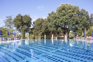 A swimming pool with blue tiles, surrounded by lounge chairs and umbrellas, with trees and a building in the background. - Appartamento Bilo Sant'Anna Pool View (Rio)