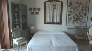 Une chambre à coucher comprenant un lit, deux chaises, une lampe, une armoire et une tapisserie à motifs floraux.