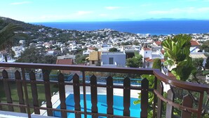 Un balcon donnant sur une ville côtière, une piscine et, au loin, une chaîne de montagnes.