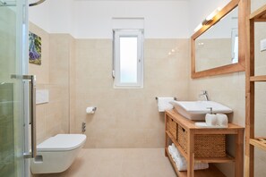 A modern bathroom with a glass shower enclosure, a white toilet, a sink with a wooden vanity, and a mirror. - Villa Mila Trogir (Seget)