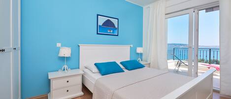 Un dormitorio con cama, mesita de noche, ventana con vista al mar y un cuadro en la pared.