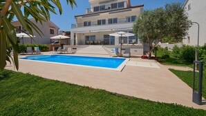 Una casa moderna de dos pisos con piscina, mobiliario exterior y un jardín bien cuidado.
