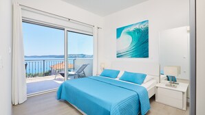 Un dormitorio con una cama grande, una mesita de noche, una silla y vista al mar a través de una puerta corredera.