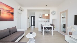 Una sala de estar moderna con un sofá, una mesa de comedor con sillas, una mesita blanca y un ventanal grande.