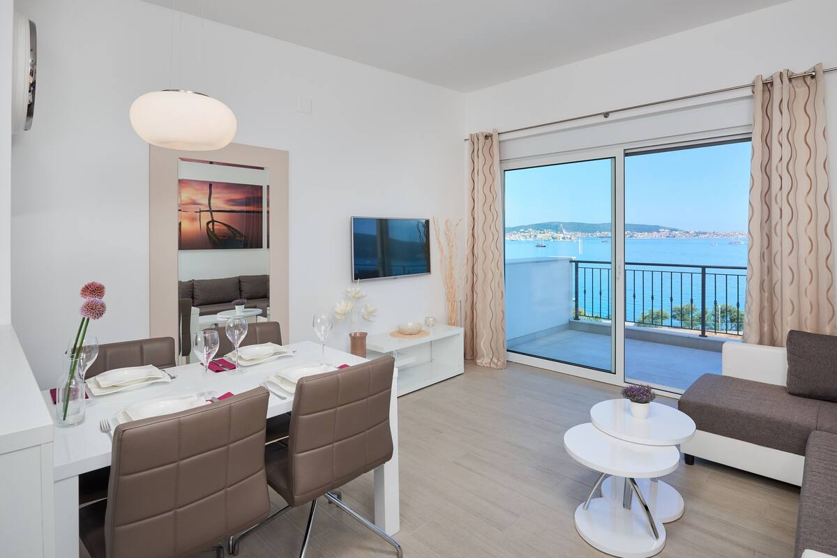 A modern living room with a balcony, a dining area, and a TV mounted on the wall.