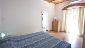 Une chambre à coucher comprenant un lit, une commode, une porte donnant sur une autre pièce et une fenêtre avec des rideaux.
