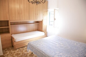 Une chambre avec un lit simple, une armoire en bois et une fenêtre.
