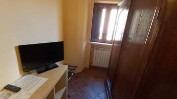 Una habitación con televisión sobre un soporte de madera, un radiador, una ventana con persianas y un armario de madera.