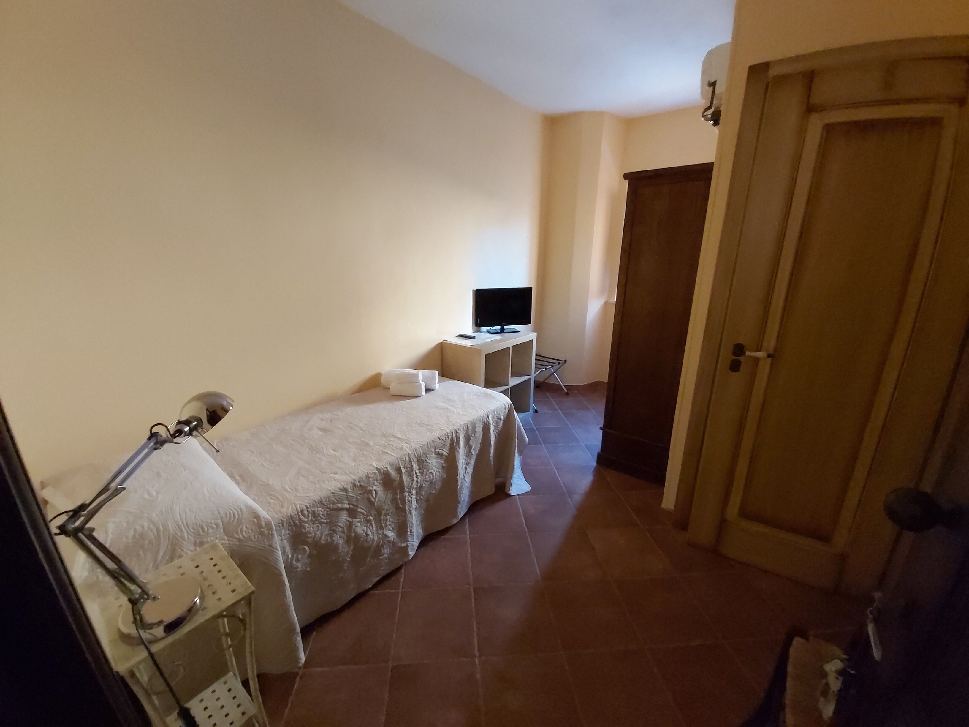 Ein Hotelzimmer mit Bett, Schreibtisch, Computer, Fernseher und einer Tür.