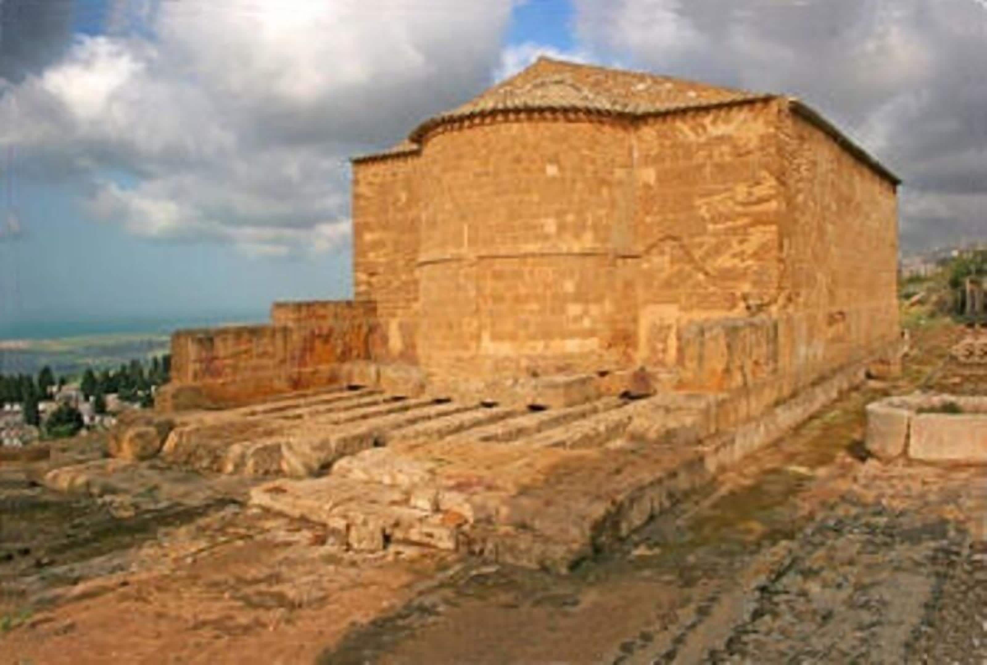 An ancient stone building with a flat roof and rectangular shape, surrounded by ruins and a clear sky.