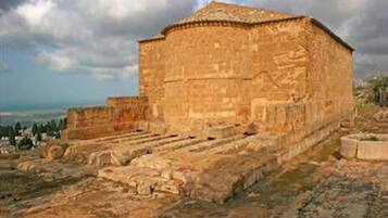 An ancient stone building with a flat roof and rectangular shape, surrounded by ruins and a clear sky.