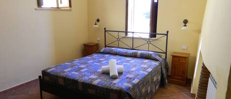 Un dormitorio con cama, ventana, mesita de noche y una lámpara de pared.