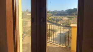 Quarto com grandes janelas que oferecem vista para área pavimentada e edifícios ao longe.