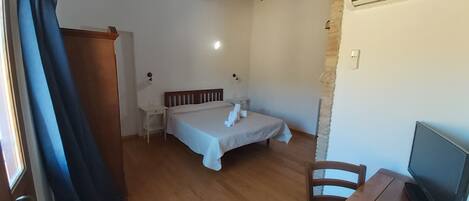 A bedroom with a bed, bedside tables, a desk with a chair, a television, and a curtain.