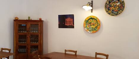 A dining area with a wooden table and chairs, a cabinet with glass doors, and two decorative plates on the wall.