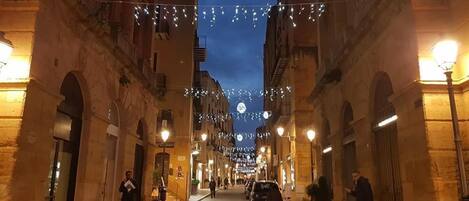 Una calle empedrada flanqueada por edificios históricos, decorada con guirnaldas luminosas y faroles.