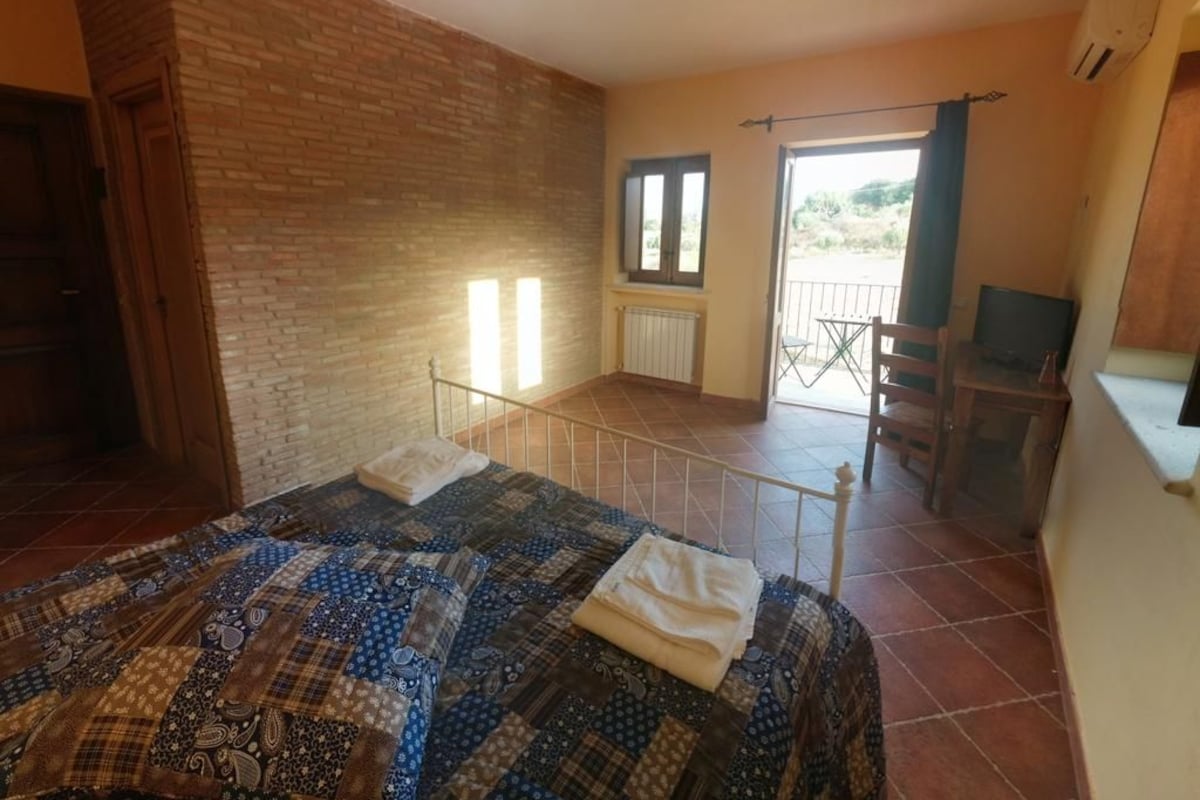 Une chambre avec une couvre-lit matelassé, un mur en briques, une fenêtre et un balcon avec une chaise.