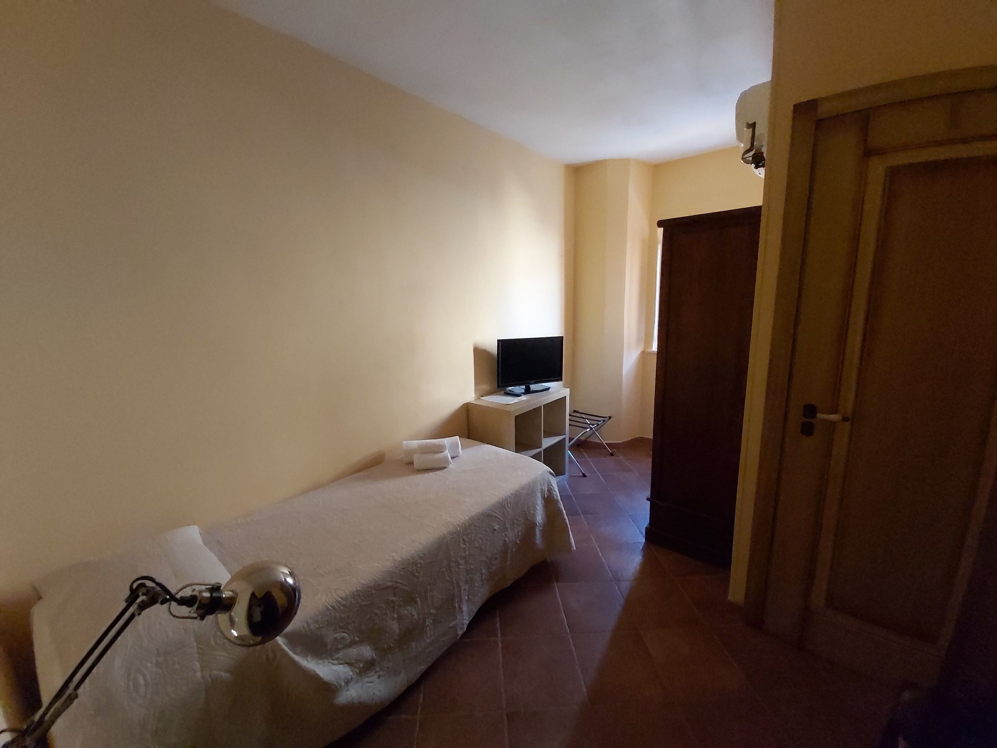 Ein kleiner, schlichter Raum mit einem Bett, einem Schreibtisch und einem Fernseher sowie einer Tür.