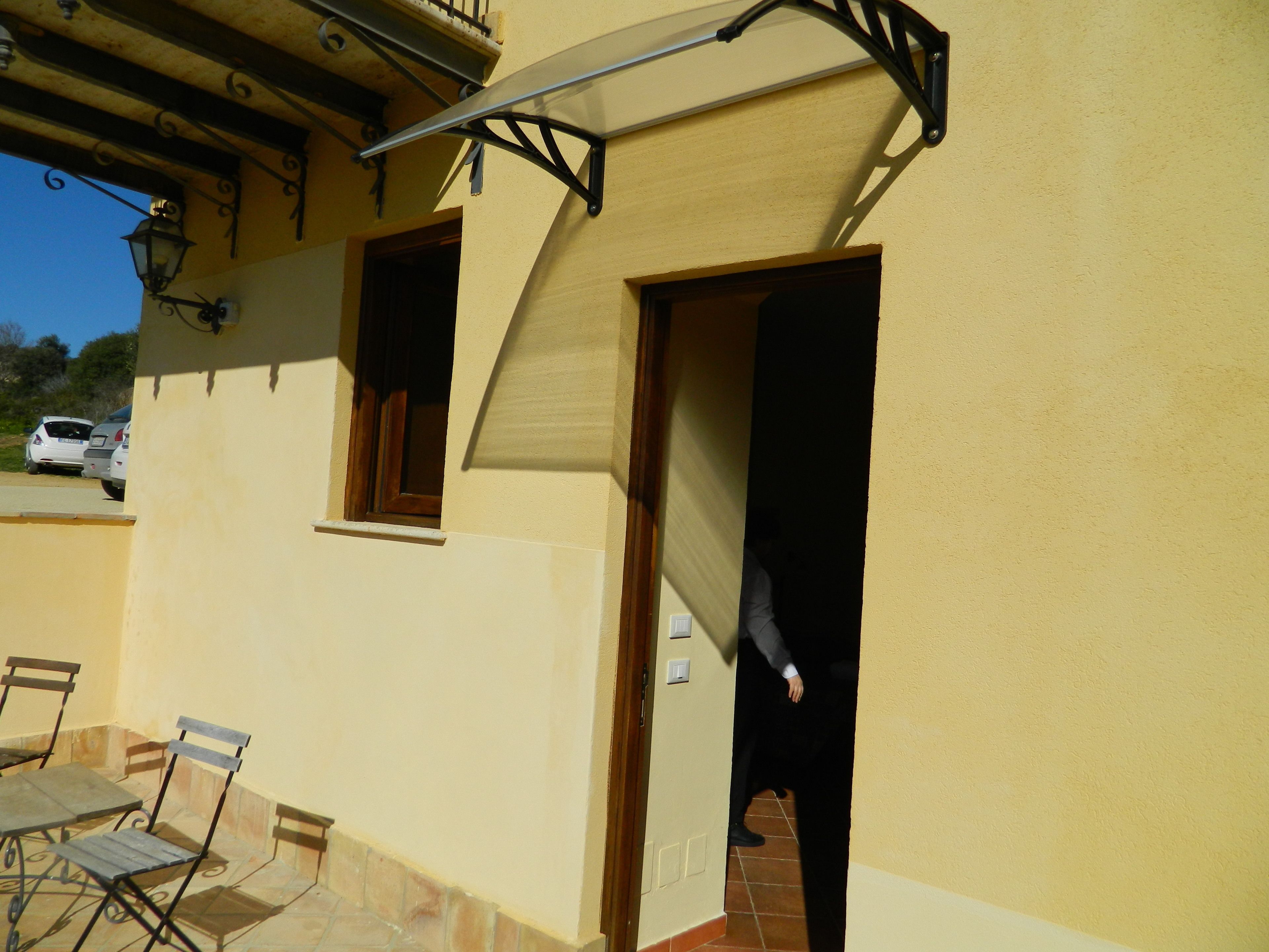 Un edificio con facciata gialla, un balcone con ringhiera in metallo e una porta che conduce a uno spazio interno.