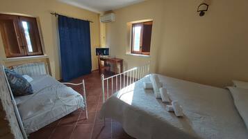 A room with two beds, a desk with a chair, an air conditioning unit, and a window with curtains.