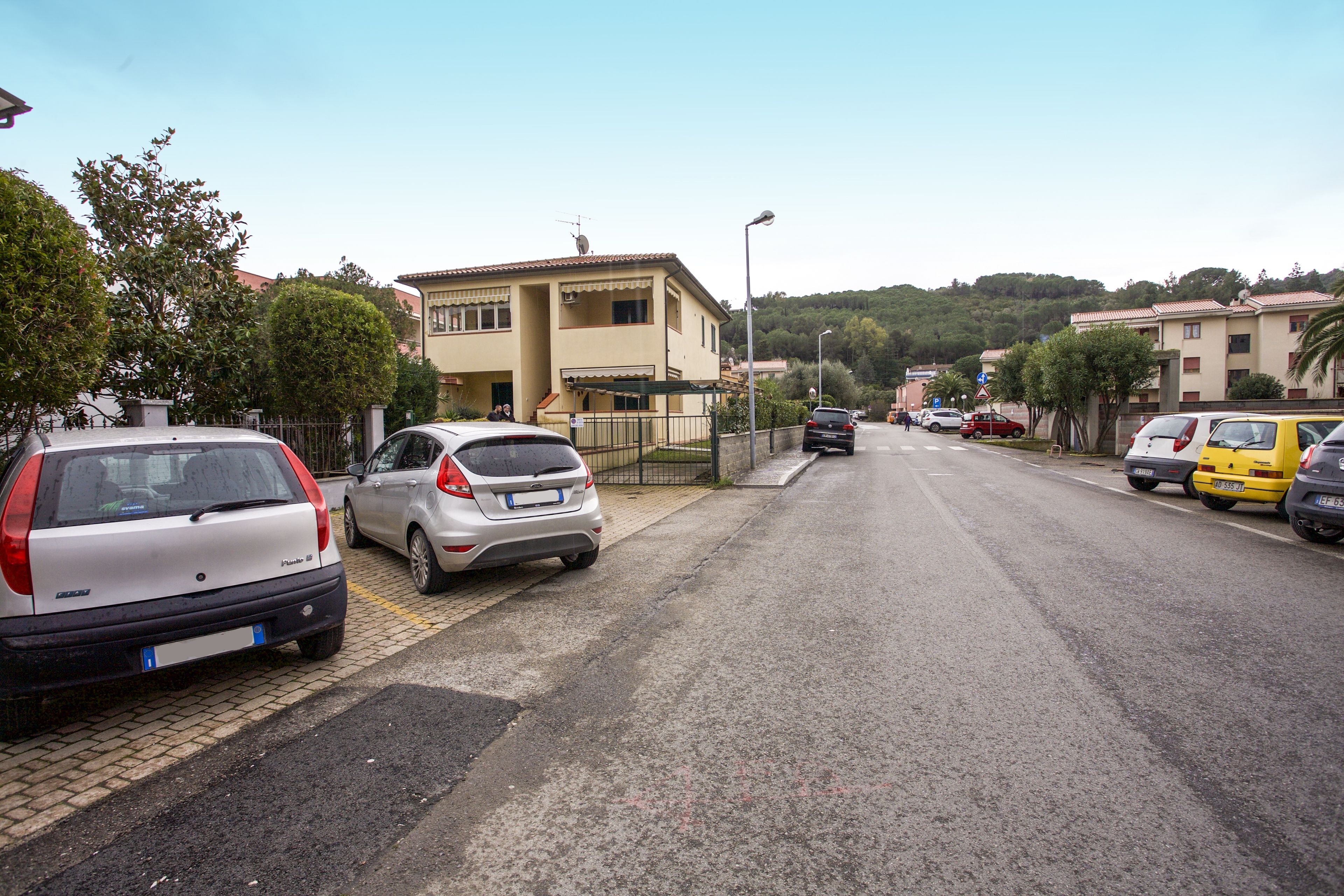 Eine Straße mit parkenden Autos, ein Gebäude mit einem Balkon und einem klaren Himmel.