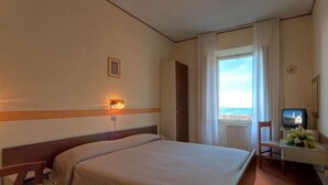 Une chambre d’hôtel avec un lit, un bureau avec une télévision, une chaise et une fenêtre avec des rideaux.