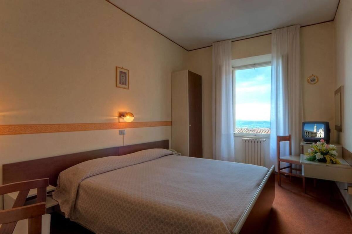 A hotel room with a bed, a desk with a television, a chair, and a window with curtains.