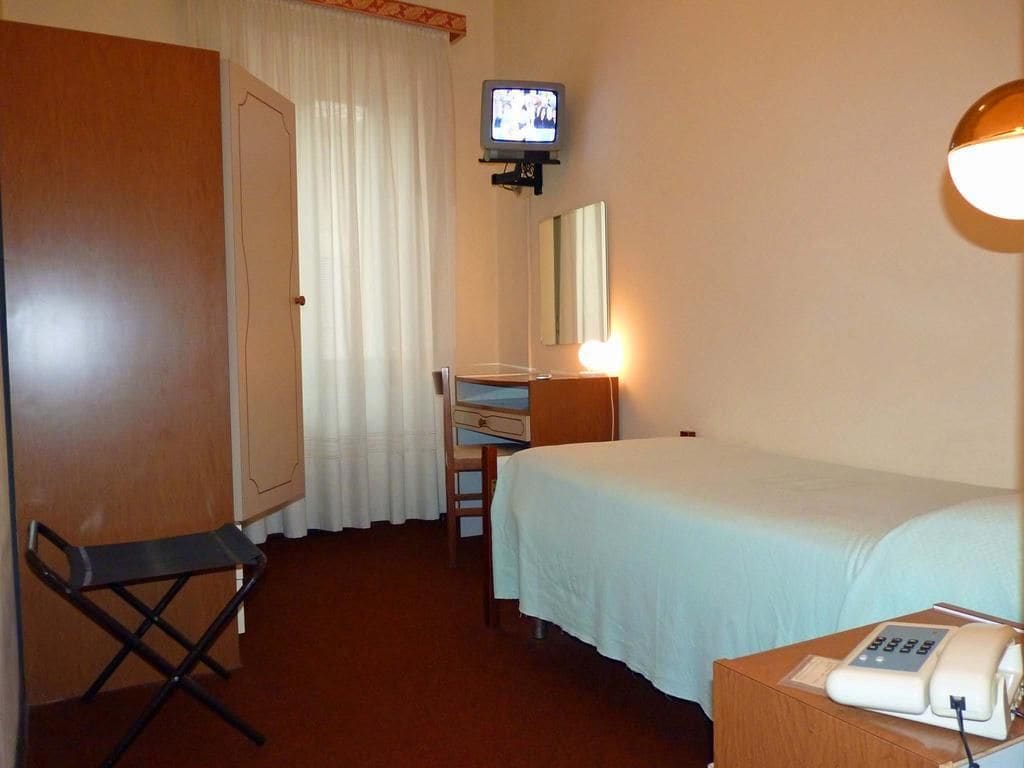 Ein Hotelzimmer mit Bett, Schreibtisch mit Stuhl, Fernseher, Spiegel und Nachttischtelefon.