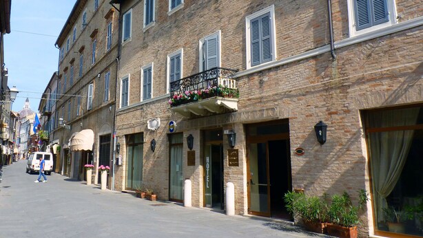 Un hôtel doté d’une façade en pierre, de nombreuses fenêtres avec volets et d’un balcon agrémenté de plantes en pot.