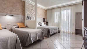A hotel room with two single beds, a large window with sheer curtains, a decorative wall panel, and a tiled floor.