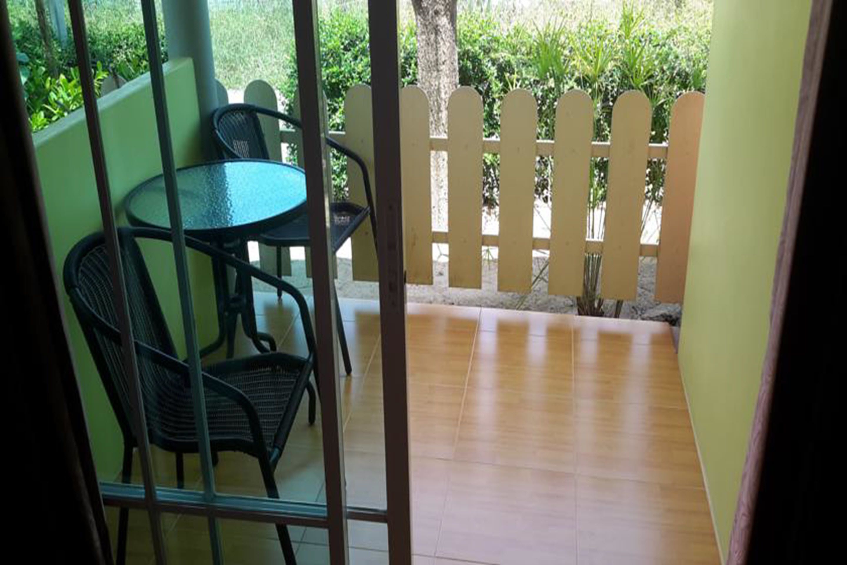 A patio area with a round table and chairs, a wooden fence, and a view of greenery.