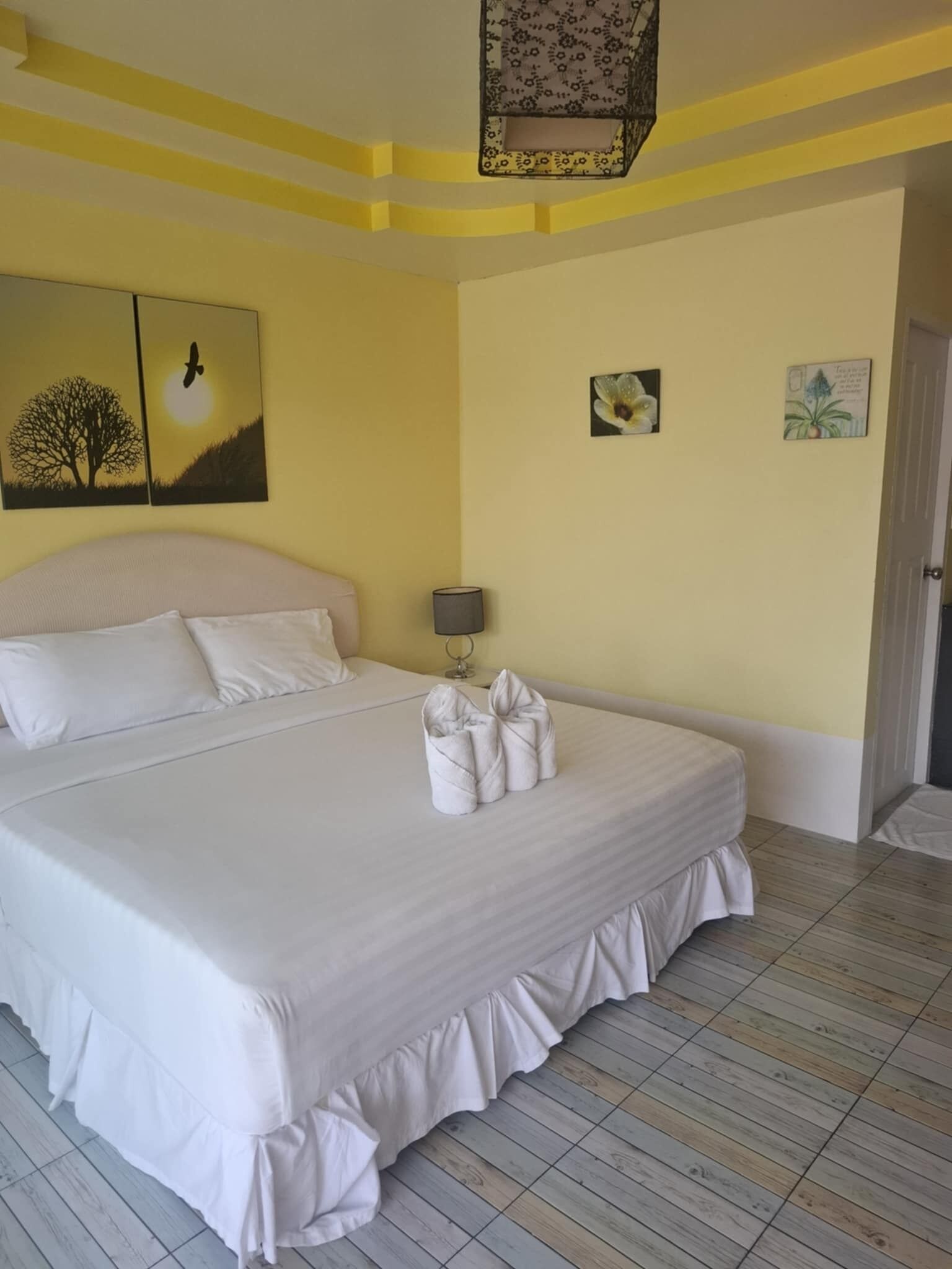 A large bed with white linens, a bedside lamp, and a floral artwork on the wall.