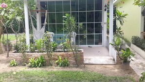 Une maison dotée d’un porche abrité, de grandes fenêtres et d’un jardin où poussent différentes espèces de plantes.