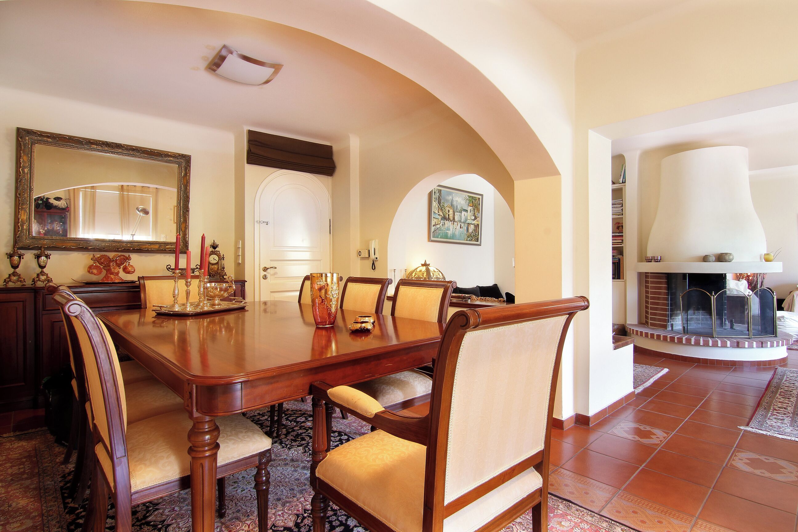 A dining area with a wooden table and chairs, a large mirror, and a fireplace.