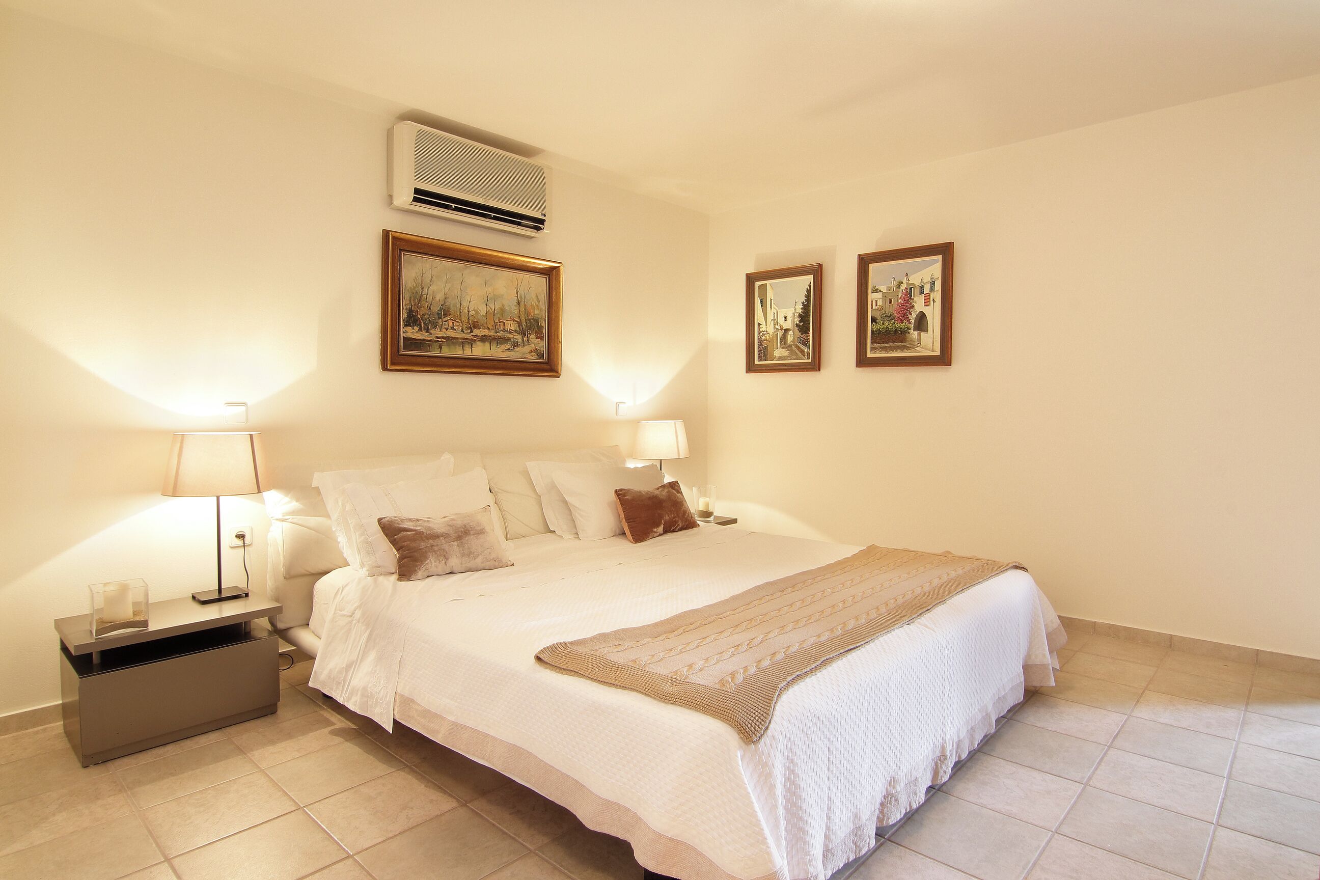 Une chambre à coucher avec un lit, des lampes de chevet, une table de chevet et des tableaux encadrés accrochés au mur.