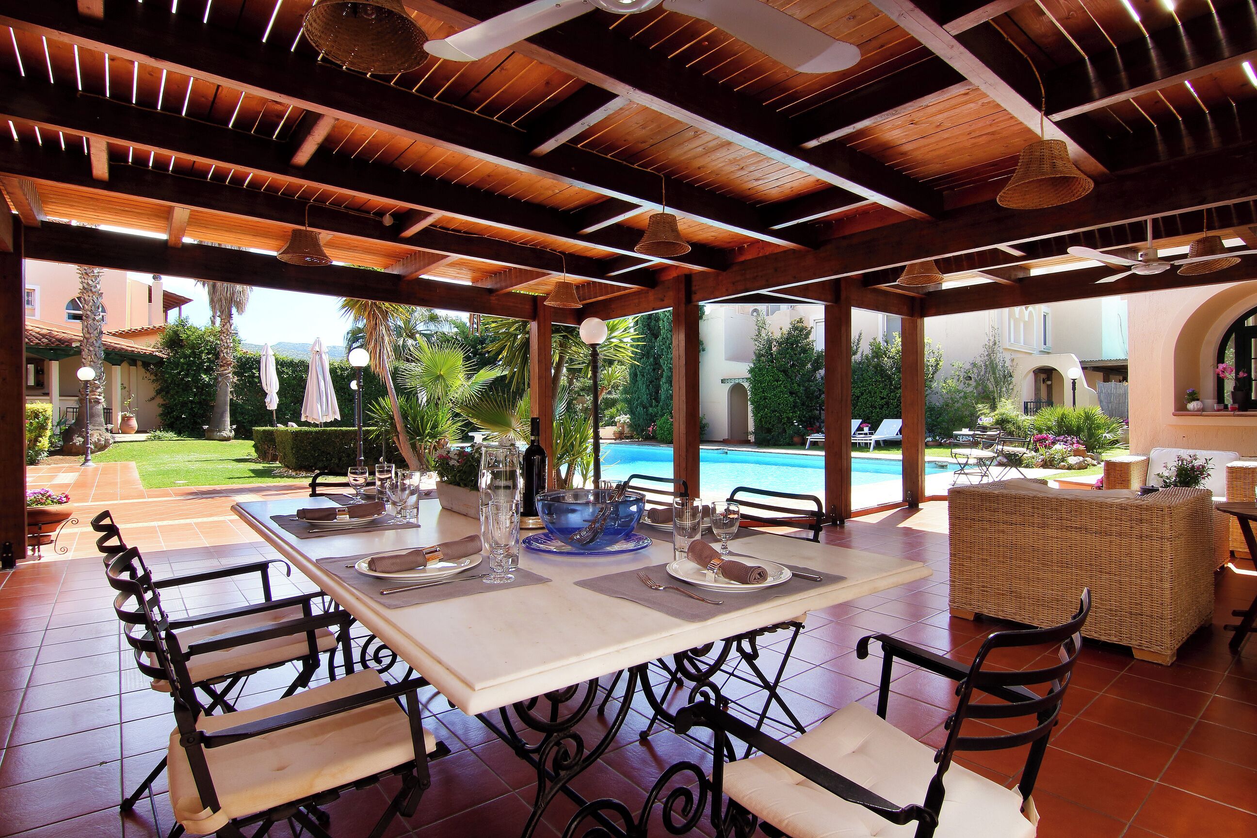 Un área de comedor al aire libre con vista a la piscina, vigas de techo de madera y mobiliario de mimbre.